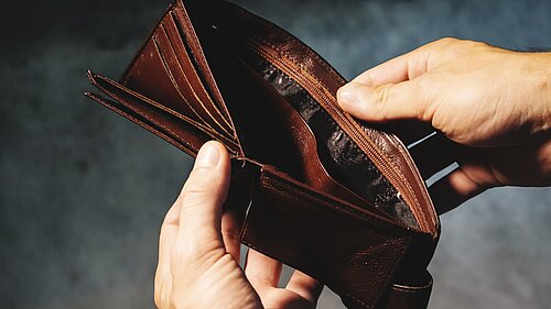 A person opening a wallet to reveal it is empty.