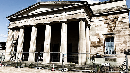Photo of the frint of the Shirehall with builders fencing